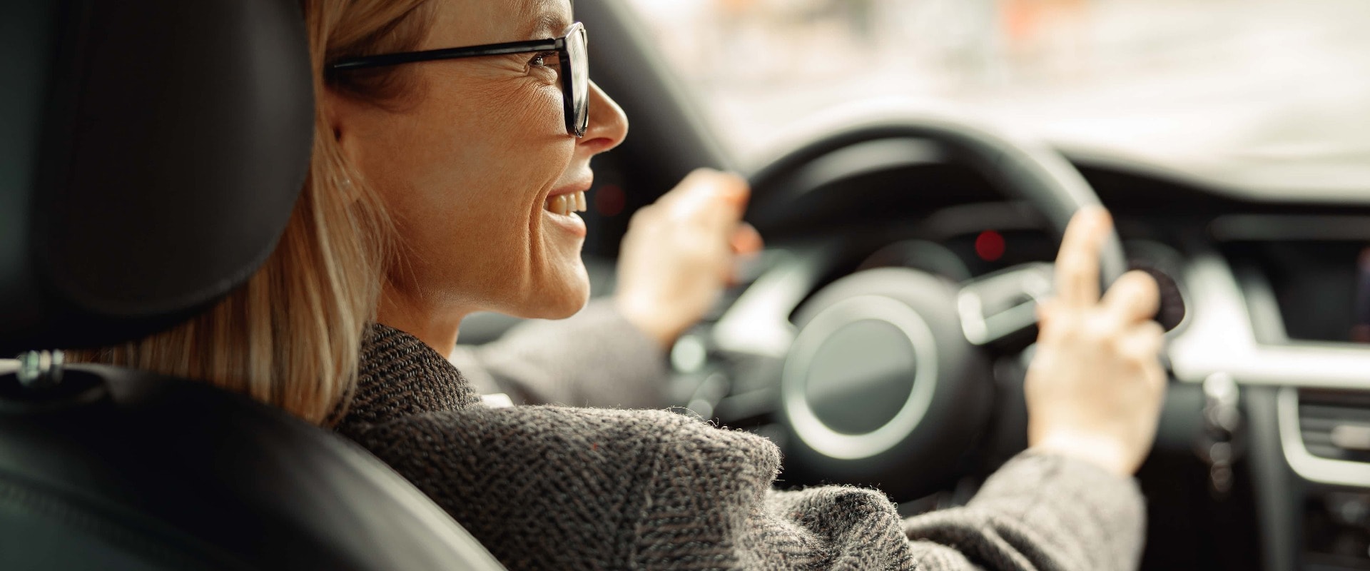 Rear view of smiling woman driving car and holding both hands on steering wheel on the way to work